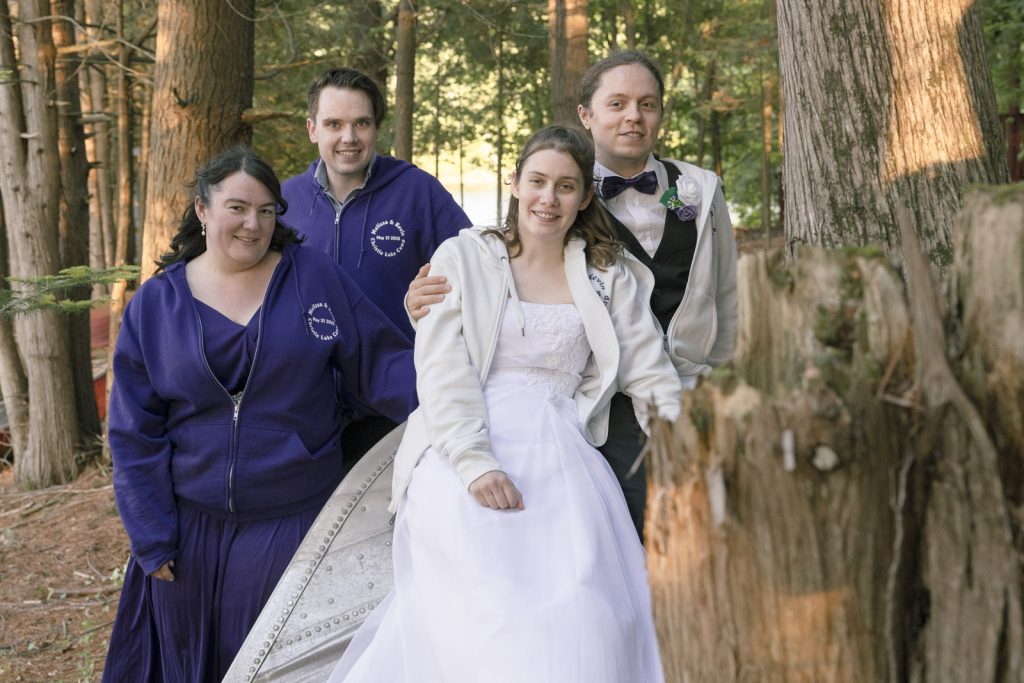 Group photo of a recently married couple and their friends sitting on an upside down boat in the woods outside Ottawa