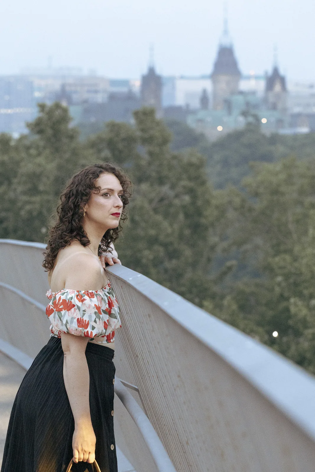 Portrait on the pedestrian footbridge at Kìwekì Point, Parliament Hill visible in the background at dusk