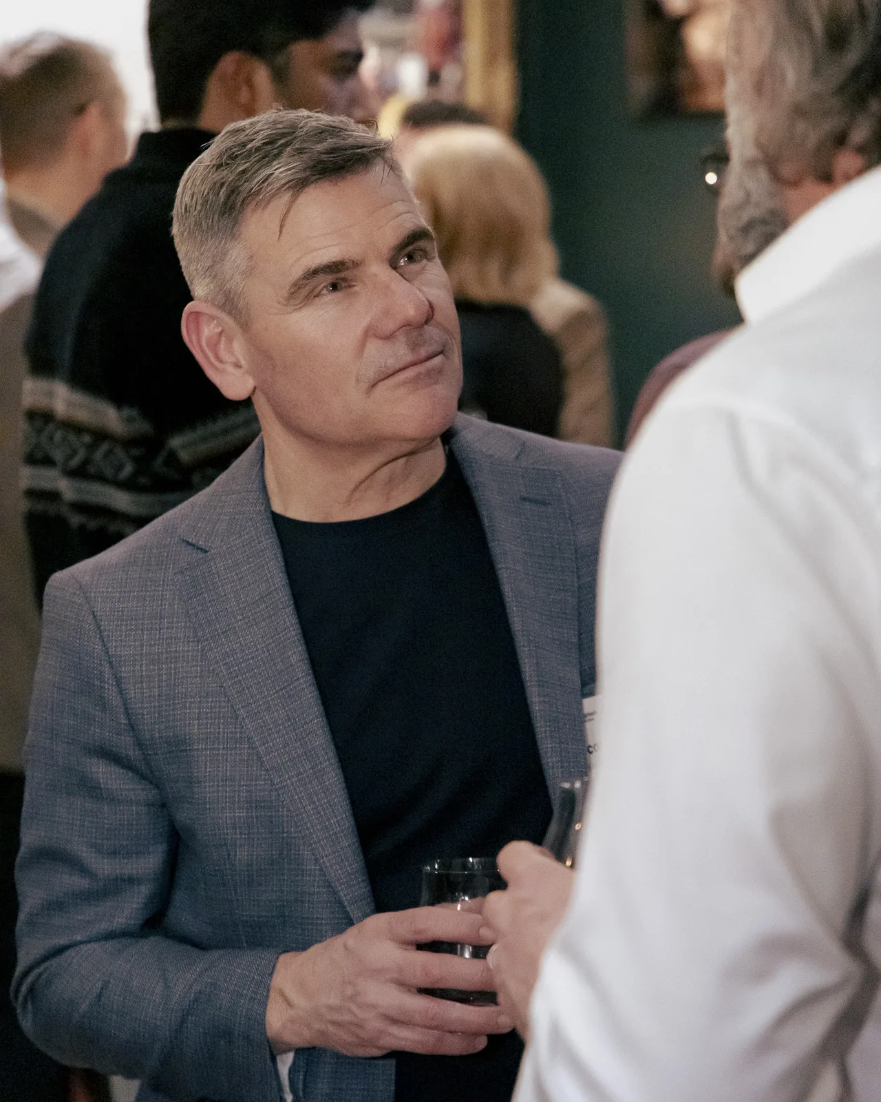 Professional networking at a Proptech Collective Ottawa event, man in grey blazer in engaged conversation with a busy room behind him