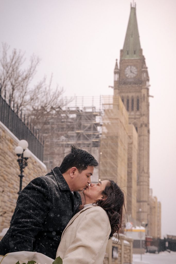Photo of a couple kissing in front of the parliament building in Ottawa after their small wedding.