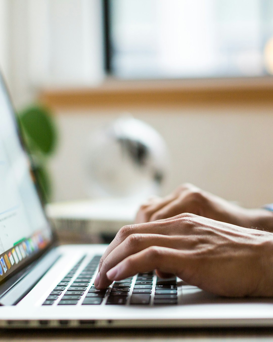 Hands typing on a laptop keyboard in a home office setting